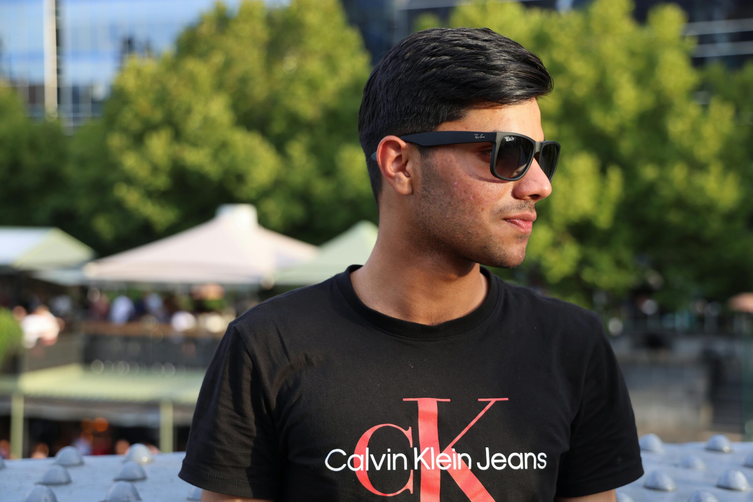A young man wearing sunglasses and a tshirt outdoors on a sunny day.
